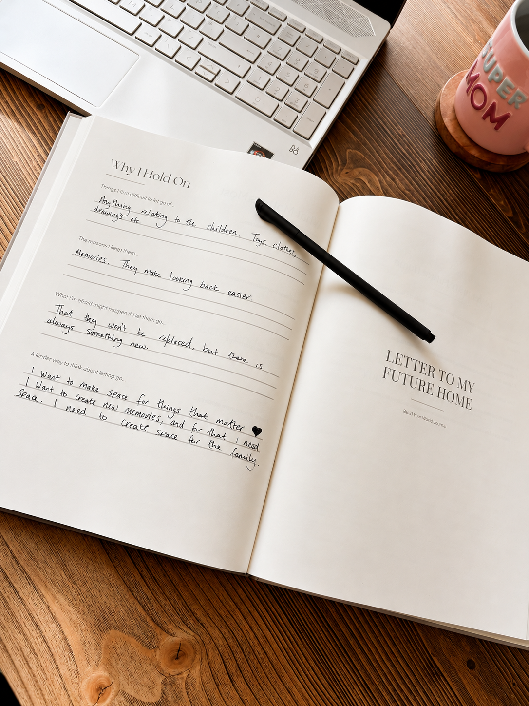 Open notebook with handwritten text on a wooden desk with a laptop and mug.